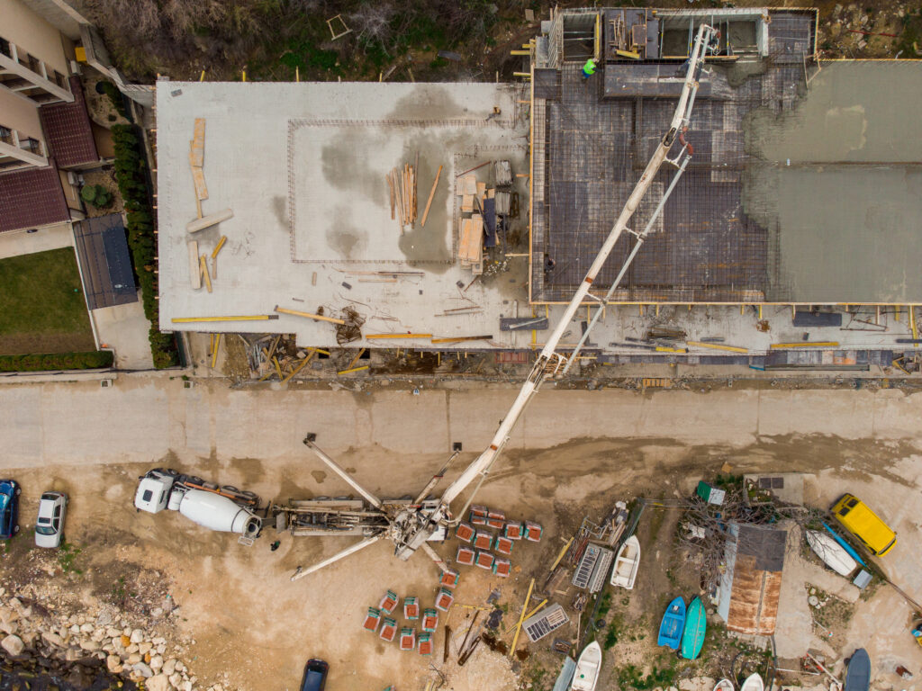 Pouring concrete cement on the roof of residential building under construction using a concrete pump truck machine with high boom to supply the mixture to the upper floors. Aerial drone view.