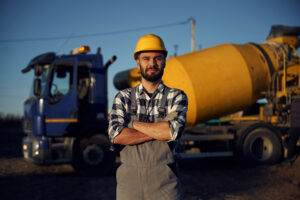 Yellow concrete mixer truck parked behind. Worker is on the construction site at daytime