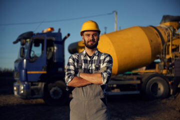 Yellow concrete mixer truck parked behind. Worker is on the construction site at daytime