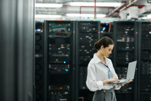 An IT specialist in a white shirt works diligently in a busy server room at a data center, handling technology.