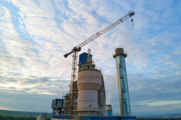 Aerial view of cement factory under construction with high concrete plant structure and tower cranes at industrial production area. Manufacture and global industry concept.