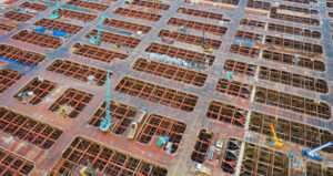 Aerial view of busy industrial under construction site workers working with cranes and excavators. Top view of precast concrete slap floor full of steel.