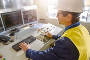 Matured man factory operator sitting at the table and working on desktop computer
